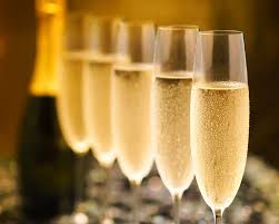 this image shows 5 glasses for prosecco filled up with a prosecco bottle in the background.