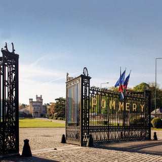 This image shows the gates of the pommery champagne house in Reims, France. the gates has a pommery sign in gold on it with two french flags attached to the gate