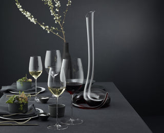 this image shows riedel decanter and glasswar set out on a table with a beautiful flower in a vase and plate and cuttlery