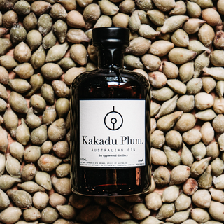 A bottle of Applewood Kakadu Plum Gin 500ml, featuring native botanicals, a black cap, and a white label, rests on a surface scattered with whole Kakadu plums.