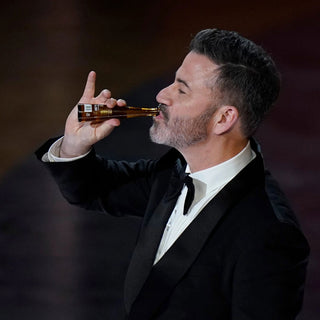 A man in a tuxedo sips Don Julio 1942 Añejo Tequila 50ml, pinky raised and eyes glancing sideways, as hints of toasted oak linger in the blurred dark background.