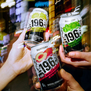 Three Suntory 196 Double Lemon, Double Grapefruit, and Double Peach & Strawberry cans held by hands against a blurred bar background.