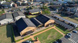 Aerial view of a building with solar panels on the roof, surrounded by other structures and vehicles.