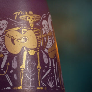 A close-up of the Clase Azul Dia de Los Muertos 2024 Música Limited Edition Tequila 1L bottle label, showcasing gold skeletons—one with a guitar and hat—on a dark background, evoking a festive Day of the Dead theme.
