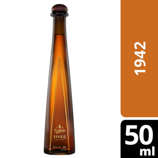 A tall, slender amber bottle of Don Julio 1942 Añejo Tequila 50ml with a dark cap features a vertical "1942" on an orange label and "50 ml" on black. Notes of caramel and toasted oak reflect its rich character.