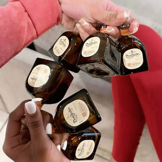 Three manicured hands raise mini bottles of Don Julio Reposado Tequila 50ml to toast. A guest in red celebrates as smooth vanilla and honeyed agave notes linger. The softly blurred background captures the festive mood.