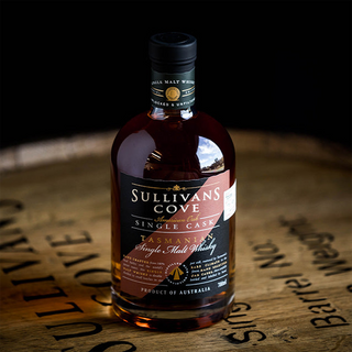 A bottle of Sullivans Cove American Oak Second-Fill TD0462 Single Malt Whisky rests on a wooden barrel, its label and dark amber liquid on display, suggesting enticing notes of orchard fruits and oak inside.