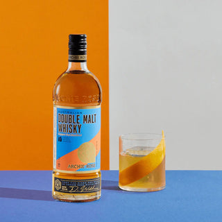 A bottle of Archie Rose Australian Double Malt Whisky stands by a whisky glass with a large orange peel garnish, set against split orange and gray backgrounds on a vibrant blue surface.