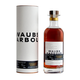 A bottle of Waubs Harbour Founders Reserve Tasmanian Single Malt Whisky is displayed beside its cylindrical packaging, both showcasing minimalist black and white labels with gold accents. The amber spirit suggests a flavor of salted pecan pie.