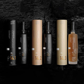 Five bottles of Octomore Edition 14.1 Single Malt Scotch Whisky, with matching cylindrical boxes, are displayed in a row on a textured black surface. Four bottles are black with metallic accents; one is light amber, suggesting peat and smoked meats.