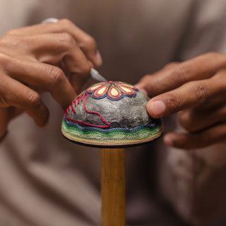Close-up of hands embroidering a vibrant floral design with pink and yellow thread on fabric, inspired by herbal patterns and smoky agave motifs featured on the Clase Azul Mezcal San Luis Potosi 750ml bottle.