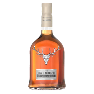 A bottle of The Dalmore King Alexander III Highland Single Malt Scotch Whisky, adorned with a silver stag emblem and front label, contains amber-hued whisky with creamy caramel and citrus zest notes, finished with a beige cap.