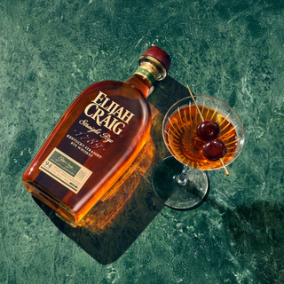 Bottle of Elijah Craig bourbon and a cocktail with cherries on a green marble surface