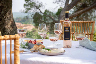 Table setting with wine glasses, a bottle of wine, and appetizers outdoors.