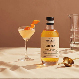 Bottle of Four Pillars Sherry Cask Gin with a cocktail and glass on a beige surface