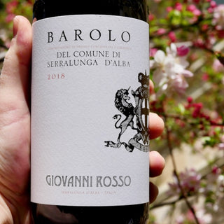 Barolo wine bottle held by a hand with a blurred floral background