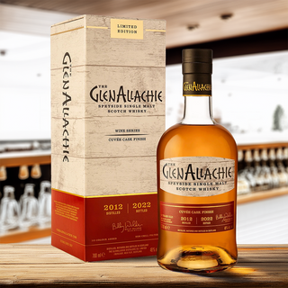 A bottle of GlenAllachie 9 Year Old Cuvée Wine Cask Single Malt Scotch Whisky and its box are shown on a wooden table, with blurred shelves in the background. This limited edition features notes of oak spice and ripe red berries.