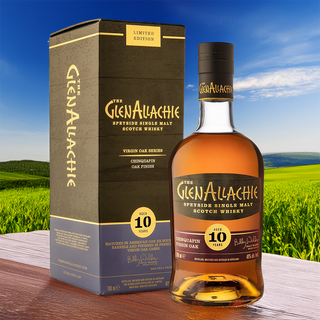 A bottle of GlenAllachie 10 Year Old Chinquapin Virgin Oak Finish Single Malt Scotch Whisky stands beside its box on a wooden surface, green hills and blue sky behind, suggesting notes of dark chocolate and caramelised fruits.