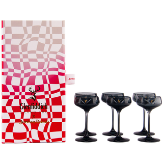 The Glenfiddich Grand Cru 23 Year Old x Jordan Dalah Box Set features a wavy-patterned gift box beside six black-stemmed cocktail glasses with gold logos, evoking notes of brioche and banana, all on a white background.