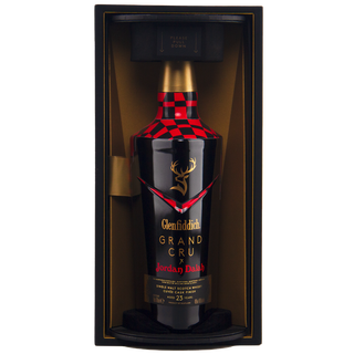 The Glenfiddich Grand Cru 23 Year Old x Jordan Dalah Box Set features a black and red bottle with a stag logo, elegantly displayed upright in a black and gold box, evoking notes of brioche and banana in its luxurious presentation.