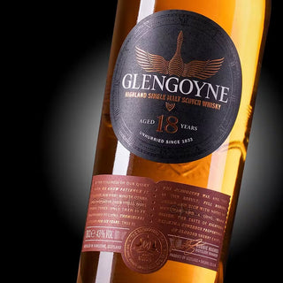 A close-up of the Glengoyne 18 Year Old Single Malt Whisky bottle label showcases gold and dark brown detailing, with amber whisky inside hinting at rich toffee and spicy oak notes visible through the clear glass.