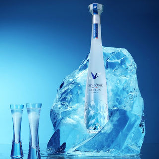 Bottle of Grey Goose Vodka surrounded by ice with two glasses on a blue background