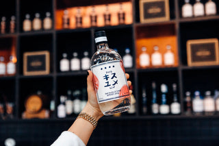 Person holding a bottle of Pilsner Urquell in front of a shelf with various bottles.