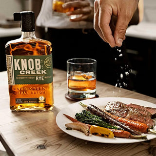 A person sprinkling salt on a plate of food, ready to enhance the flavors just as Knob Creek Kentucky Straight Rye Whiskey adds depth and character to every sip.