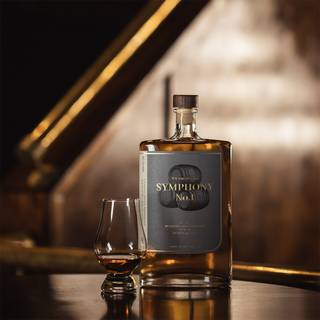 A bottle of Lark Symphony No.1 Tasmanian Whisky and a whiskey glass with a small pour rest on a polished wooden surface, with notes of honey and dried fruits lingering in the blurred golden-brown background.