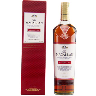 A bottle of The Macallan Classic Cut 2019 Release Single Malt Scotch Whisky stands by its red, textured box with gold and white labels. Hints of orange zest and oak spice reflect the whisky’s sophisticated branding and refined taste.