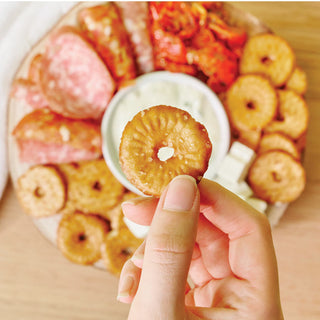 Hand holding a small round pretzel with a plate of assorted pretzels and charcutuerie in the background