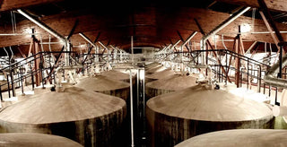 Large wooden vats in a warehouse setting with wooden beams and lighting fixtures.