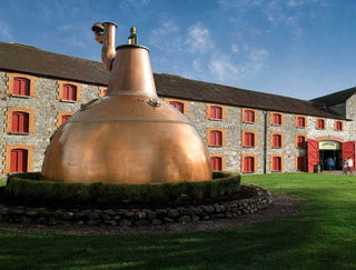 Large copper still in front of a stone building with red windows