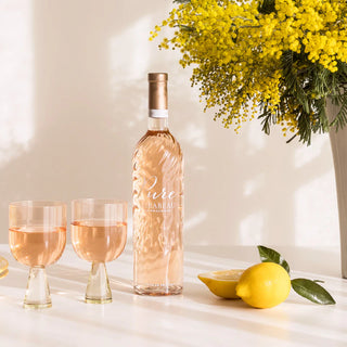 Bottle of rose wine with two glasses, lemons, and a bouquet of yellow flowers on a light surface.