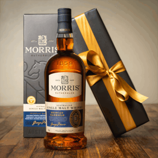 A bottle of Morris Whisky Muscat Barrel Australian Single Malt Whisky stands before its branded box and a gold-ribboned gift box on a wooden surface, evoking notes of sweet malt and dried figs.
