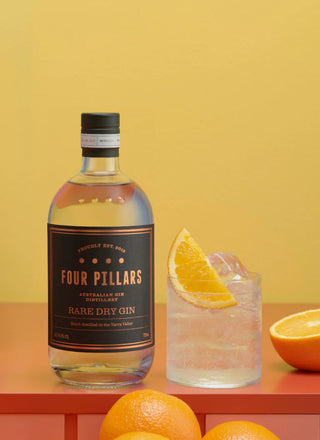 Four Pillars Rare Dry Gin bottle with a cocktail and oranges on a yellow background