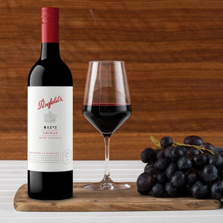 Penfolds wine bottle with a glass of red wine and grapes on a wooden surface