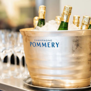 Champagne bottles in an ice bucket with 'Pommery' branding, surrounded by glasses.