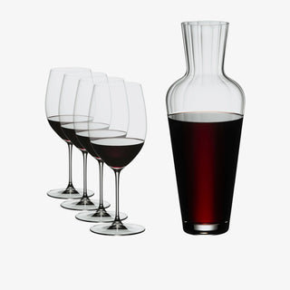 A clear glass decanter filled with red wine stands beside four matching wine glasses, each partially filled with red wine, on a light gray background.