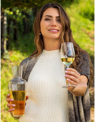 Woman holding a glass of white wine and a carafe in an outdoor setting