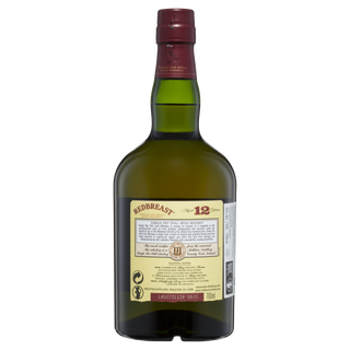 A green glass bottle of Redbreast 12 Year Old Single Pot Still Irish Whiskey with a red cap displays the back label—this classic spirit is known for sherried sweetness and notes of dried fruits.