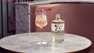Bottle of gin and a glass of cocktail on a marble table with floral decoration.