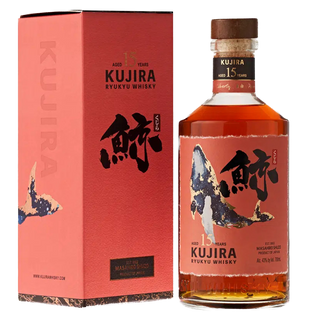 A bottle of Kujira Ryukyu 15 Year Old Japanese Whisky stands beside its matching red and black box, both adorned with striking Japanese calligraphy and a whale design, suggesting notes of tropical fruit and butterscotch.