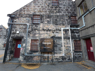 Grayscale image of a stone building with 'Tamdhu' sign on a street.