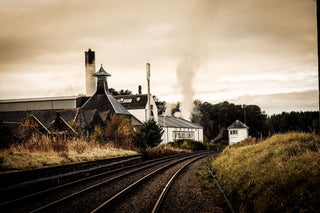 Factory or industrial building with smokestacks and train tracks in the foreground.