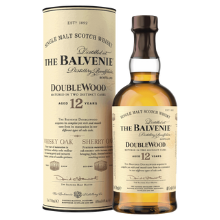 A bottle of The Balvenie DoubleWood 12 Year Old Single Malt Scotch Whisky stands beside its cylindrical package, both featuring beige labels with black text detailing its oak cask aging and notes of honey.