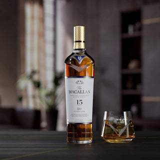 A bottle of The Macallan Double Cask 15 Year Old Single Malt Scotch Whisky sits beside a whisky glass on a dark table, evoking notes of dried fruit and creamy vanilla, with a blurred modern room in the background.