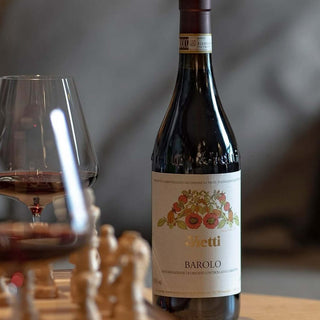 Bottle of Vetti Barolo wine with a glass of wine on a wooden stand.