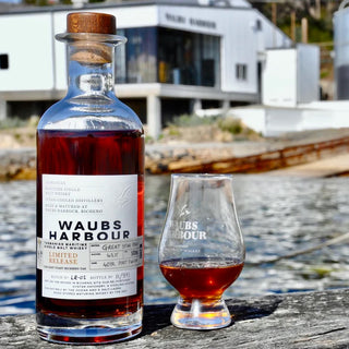 Bottle and glass of Waubs Harbour whisky on a wooden surface with a blurred background