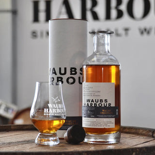Waubs Harbour whisky bottle, glass, and canister on a wooden surface with blurred background.